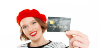 smiling-ginger-woman-showing-credit-card-camera-grey-focus-card